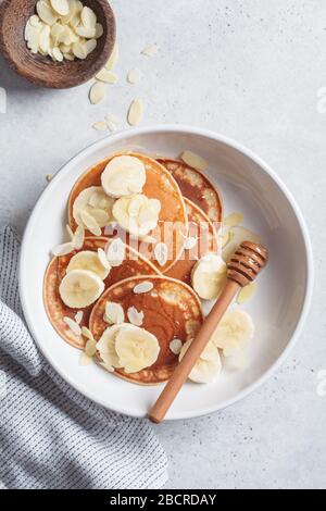 Pancake tradizionali con banana, mandorle e miele in un piatto bianco. Foto Stock