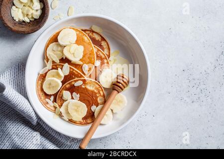 Pancake tradizionali con banana, mandorle e miele in un piatto bianco. Foto Stock