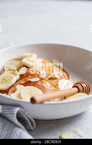 Pancake tradizionali con banana, mandorle e miele in un piatto bianco. Foto Stock