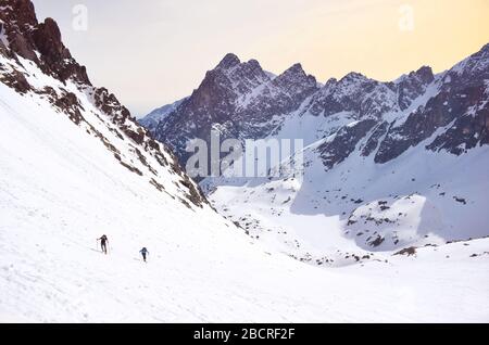 Due sciatori che camminano su una collina in grandi montagne coperte di neve - bella valle sullo sfondo Foto Stock