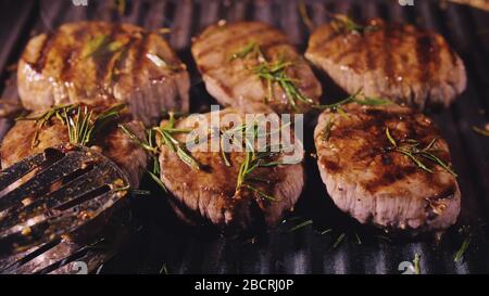 Deliziosa bistecca di carne succosa alla griglia. Manzo di marmo arrosto di prima cottura invecchiato. Torrefattore elettrico, pepe nero al rosmarino, sale. Pinze da cucina. Foto Stock