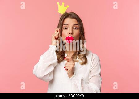 Primavera, felicità e celebrazione concetto. Ritratto ravvicinato di ragazza bionda divertente e carina in abito bianco, con maschera e corona di labbra grandi Foto Stock