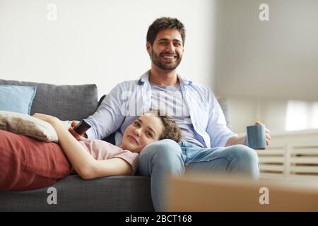 Ritratto di coppia felice guardare la TV insieme mentre si siede sul divano a casa in accogliente appartamento godendo il tempo pigro, copia spazio Foto Stock