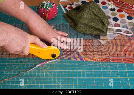 Le mani della donna con un taglierino rotante per tagliare il tessuto trapuntato rimasto per maschere facciali cucite a mano Foto Stock