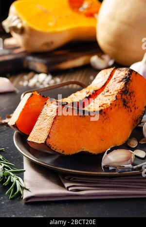 Fette di zucca al forno su vassoio di metallo sulla cucina rustica tavolo di legno con spicchi d'aglio e rosmarino Foto Stock