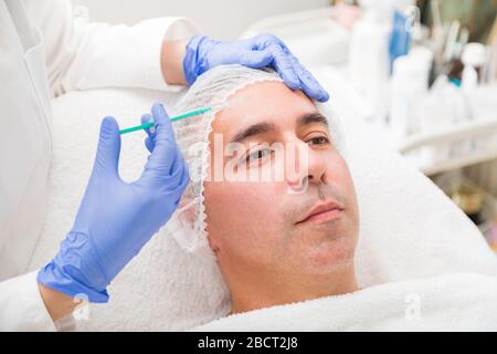 L'uomo riceve l'iniezione ringiovanente sulla fronte nel salone medico Foto Stock