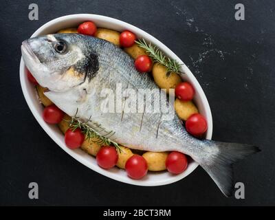 orata, tomatos, potatos e rosmarino su un piatto di portata su fondo ardesia. pronto per cucinare. vista dall'alto Foto Stock