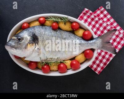 orata, tomatos, potatos e rosmarino su un piatto di portata su fondo ardesia. pronto per cucinare. vista dall'alto Foto Stock