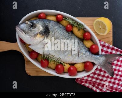 orata, tomatos, potatos e rosmarino su un piatto di portata su fondo ardesia. pronto per cucinare. vista dall'alto Foto Stock