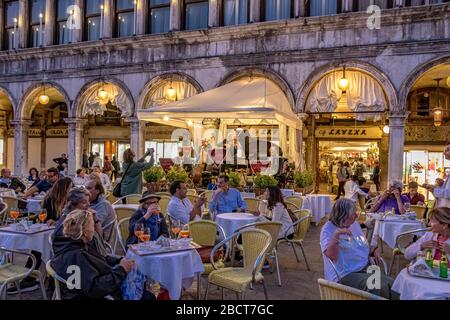 Persone sedute fuori caffè Lavena in Piazza San Marco in prima serata ascoltando la band residente suona, Venezia, Italia Foto Stock