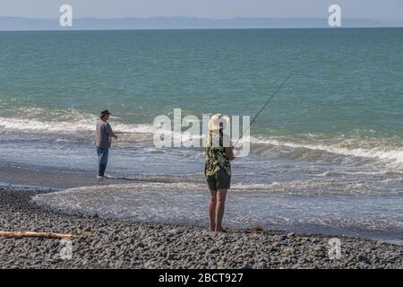 Uomo e donna che pescano sul bordo del mare a Hawkes Bay, Nuova Zelanda Foto Stock