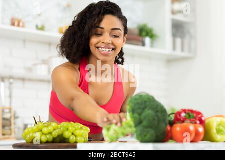 Felice giovane donna nera che prepara insalata di verdure Foto Stock