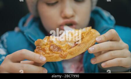 Bambino mangiare pizza formaggio quattro. Primo piano di ragazza giovane donna mangiare pizza e masticare in ristorante all'aperto. Bambini mani prendere pezzo pizza. Foto Stock