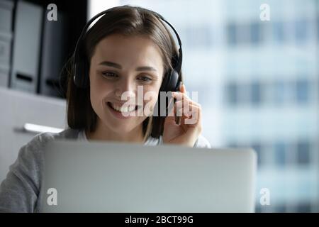 Donna sorridente in cuffie che lavora su un notebook in ufficio Foto Stock