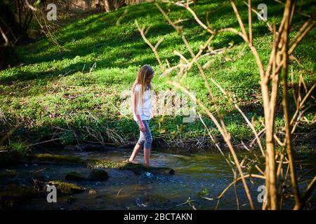 Bambino cute ragazza bionda coraggiosa che gioca nel torrente. Ragazza coraggiosa che cammina nel torrente della foresta ed esplora la natura. Divertimento estivo per i bambini. Bambini estate Foto Stock