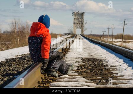 Il bambino è seduto sulle rotaie della ferrovia. In attesa del treno Foto Stock