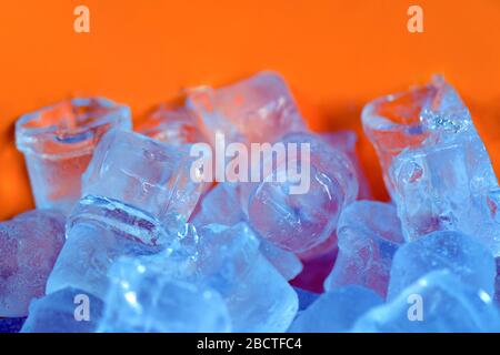 molti pezzi di ghiaccio di diverse forme giacciono su fondo arancione. ghiaccio per i coccodri. ghiaccio per raffreddare le bevande alcoliche Foto Stock