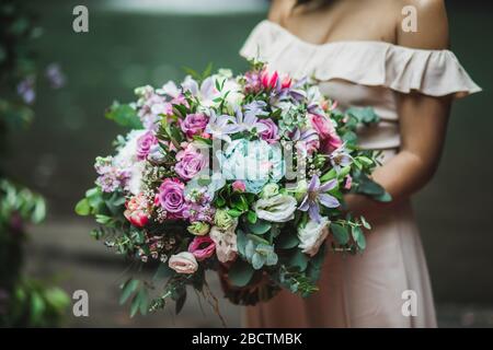 Sposa tenuta in mano incredibile bouquet fiorente enorme sulla cerimonia di nozze. Rosa rose, peonia, tulipani rossi e verdi primo piano. Foto Stock