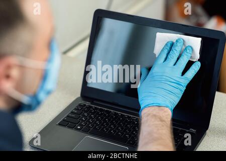 Uomo che disinfetta il laptop prima di lavorare seduto a casa, retro-vista, ritagliato Foto Stock