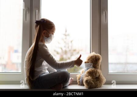 Triste bambino e il suo orso di teddy entrambi in maschere mediche protettive. Bambini e malattie COVID-2019 concetto di malattia Foto Stock