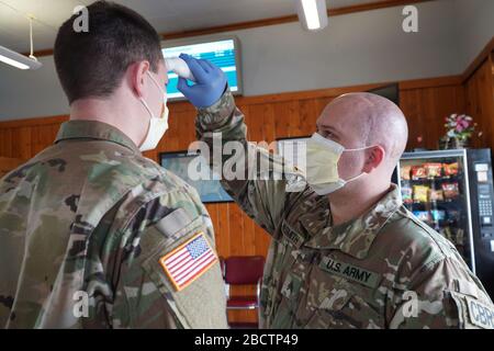 Esercito Sgt. Willy Nesmith con la 631st Chemical Company di Cut Bank, Montana, prende la temperatura di Army SPC. Trevor Dodson con il 1-189th GSAB da Shelby, Montana, come parte della verifica quotidiana del benessere personale presso la stazione ferroviaria Amtrak a Shelby, Montana, 3 aprile 2020. 73 Montana Army and Air National Guard uomini e donne sono stati attivati per lo stato Active Duty dal governatore Steve Bullock per schermare 17 posizioni intorno allo stato nel tentativo di appiattire la curva in Montana. (STATI UNITI Foto della Guardia Nazionale aerea del personale Sgt. Brandy Burke) Foto Stock