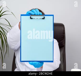 mani del medico in guanti blu in lattice medico tiene una cartella con una graffetta, luogo per la scrittura di una diagnosi, messaggio Foto Stock