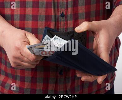 Uomo in una camicia rossa a scacchi tiene un portafoglio pieno di cento banconote da dollari USA, concetto di stipendio, ricchezza Foto Stock