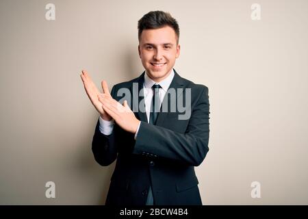 Giovane e bel uomo d'affari che indossa un abito elegante e cravatta su sfondo isolato applappando e applaudendo felice e gioioso, sorridendo orgogliosi mani insieme Foto Stock