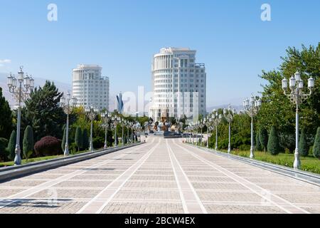 Independence Park fiancheggiata da pavimenti e pali luminosi ornati ad Ashgabat, Turkmenistan. Saparmurat Niyazov statua dorata e edifici in marmo bianco Foto Stock