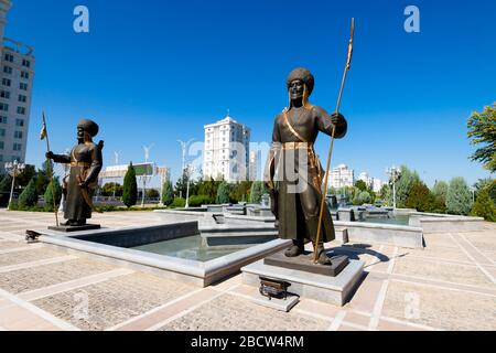 Statua di soldati in bronzo nel Parco dell'Indipendenza di Ashgabat, Turkmenistan. Edifici in marmo bianco visibili dietro sculture e fontana d'acqua. Foto Stock