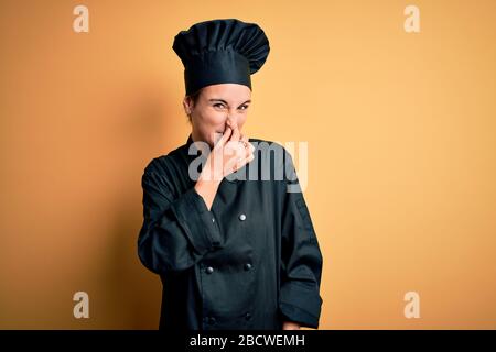 Giovane e bella chef donna indossare cucina uniforme e cappello in piedi su sfondo giallo odore qualcosa di puzzolente e disgustoso, odore intollerabile, Foto Stock