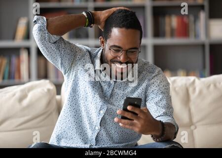 Sorridente afro americano uomo leggere buone notizie su cellulare Foto Stock