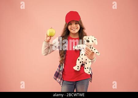 Apple è una buona fonte di vitamina C. Felice piccolo bambino di tenere la vitamina frutta su sfondo rosa. Bambina con vitamina sani snack. Vantaggi della vitamina a mangiare cibo per bambini attività. Foto Stock