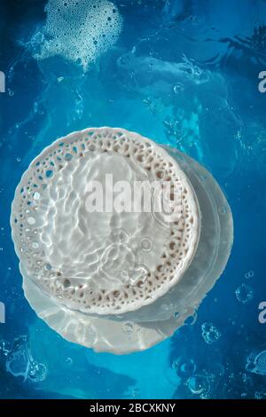 Piatti e piatti in porcellana imbevuti d'acqua con onde e increspature, concetto di piatti da fare Foto Stock