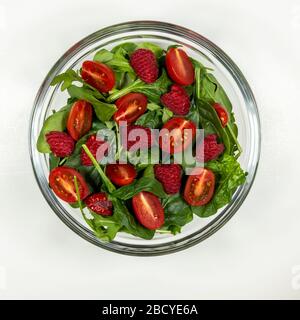 Piatto di insalata di verdure fresche. Ingredienti: Miscela primavera verde, pomodori ciliegini, lamponi, cipolla, formaggio feta, condimento. Fase 3 - lamponi. Foto Stock