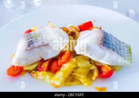 spigola al forno con verdure fritte e pomodori ciliegini saltati con erbe aromatiche Foto Stock