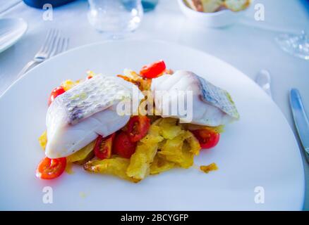 spigola al forno con verdure fritte e pomodori ciliegini saltati con erbe aromatiche Foto Stock