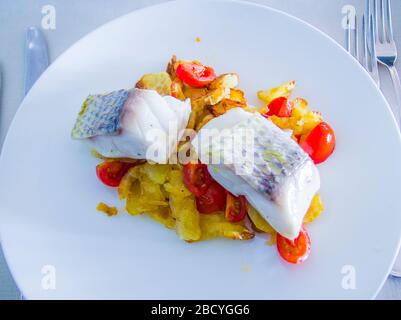 spigola al forno con verdure fritte e pomodori ciliegini saltati con erbe aromatiche Foto Stock