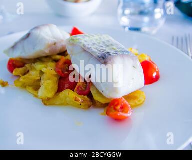 spigola al forno con verdure fritte e pomodori ciliegini saltati con erbe aromatiche Foto Stock