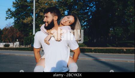 Uomo barbuto in abiti bianchi che porta la sua ragazza e sorridente fuori in strada Foto Stock