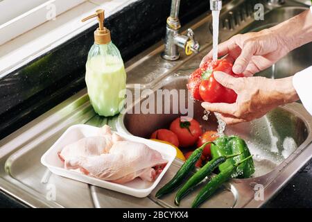 Uomo maturo che sciacqua le verdure sotto l'acqua del rubinetto nel lavello della cucina Foto Stock