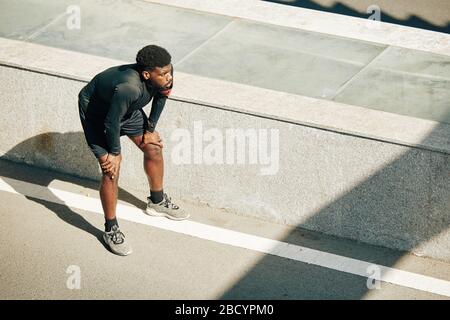 Sportivo stanco che si appoggia sulle ginocchia e ha un breve riposo dopo il jogging all'aperto Foto Stock