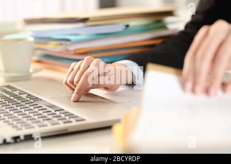 Primo piano di una donna dirigente lavorata che controlla i documenti utilizzando il laptop su una scrivania in ufficio Foto Stock