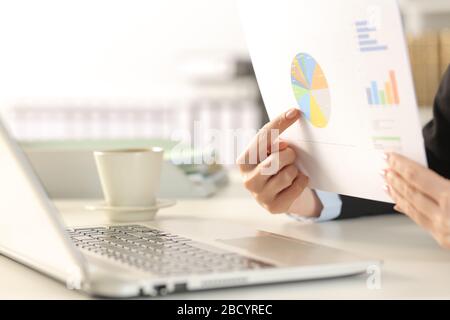 Primo piano delle mani di una donna dirigente che effettua una videochiamata mostrando i grafici sulla webcam del notebook che si trova su una scrivania in ufficio Foto Stock