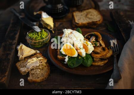 Colazione appetitosa uova sode, toast, formaggio e funghi in un piatto di argilla su un fondo di legno. Uovo medio cotto. Foto Stock