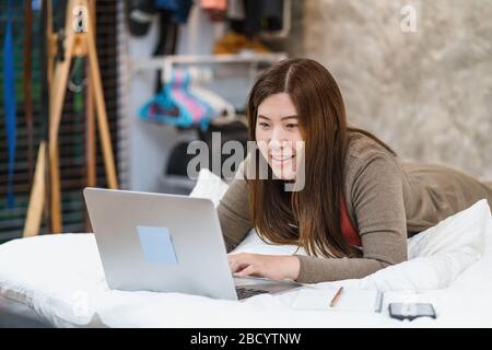 Donna asiatica d'affari che utilizza la tecnologia notebook e di lavoro da casa in camera da letto al coperto, freelance e imprenditore, startup e imprenditore, stile di vita Foto Stock
