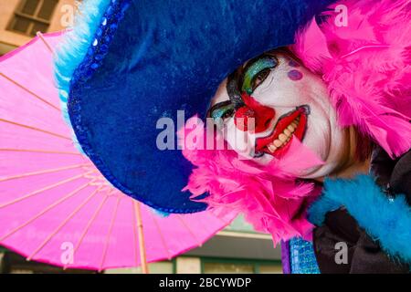 Una donna, vestita e dipinta come un clown, si sta sfilando per le strade durante il Carnevale di giorno Foto Stock