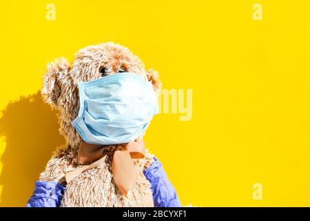 Coronavirus covid-19 e antinquinamento concetto. Orso bambola teddy indossare maschera e guanti protettivi su sfondo giallo, spazio copia Foto Stock