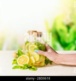 Donna femmina bottiglia mano con zenzero, limone, menta limonata su tavolo bianco su sfondo verde natura. Bevande estive salutari. Immun naturale boo Foto Stock