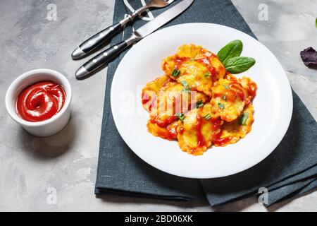 Ravioli con salsa di pomodoro e basilico su fondo in cemento. Pasta deliziosa Foto Stock